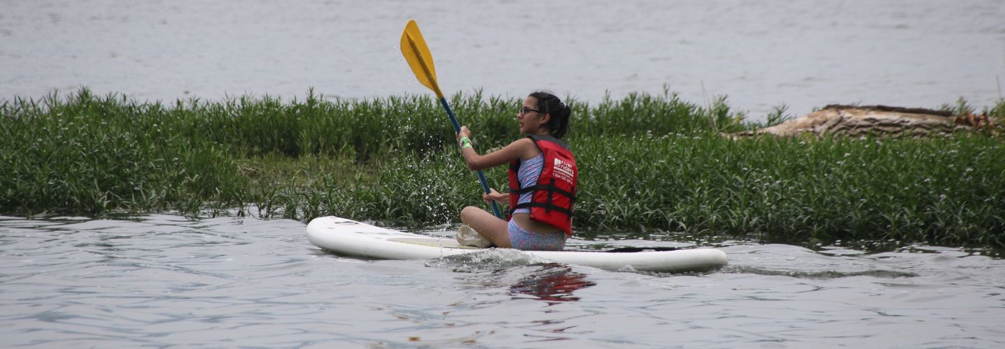 girl sitting on a paddleboard rental cross-legged paddling across the water