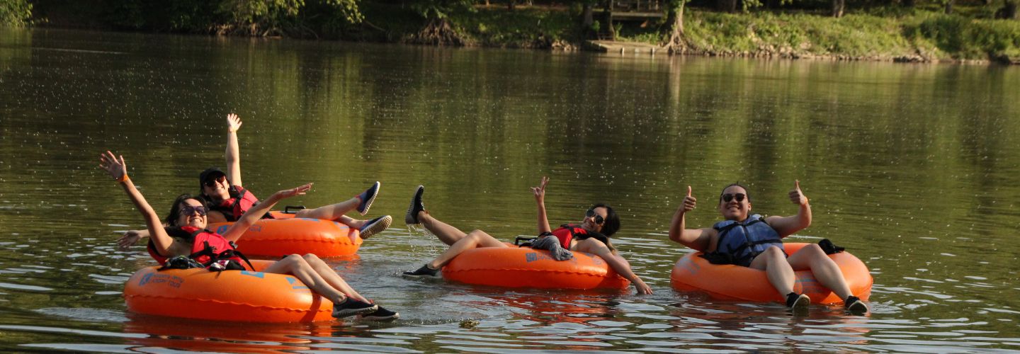 4 friends floating on flat water in tubes