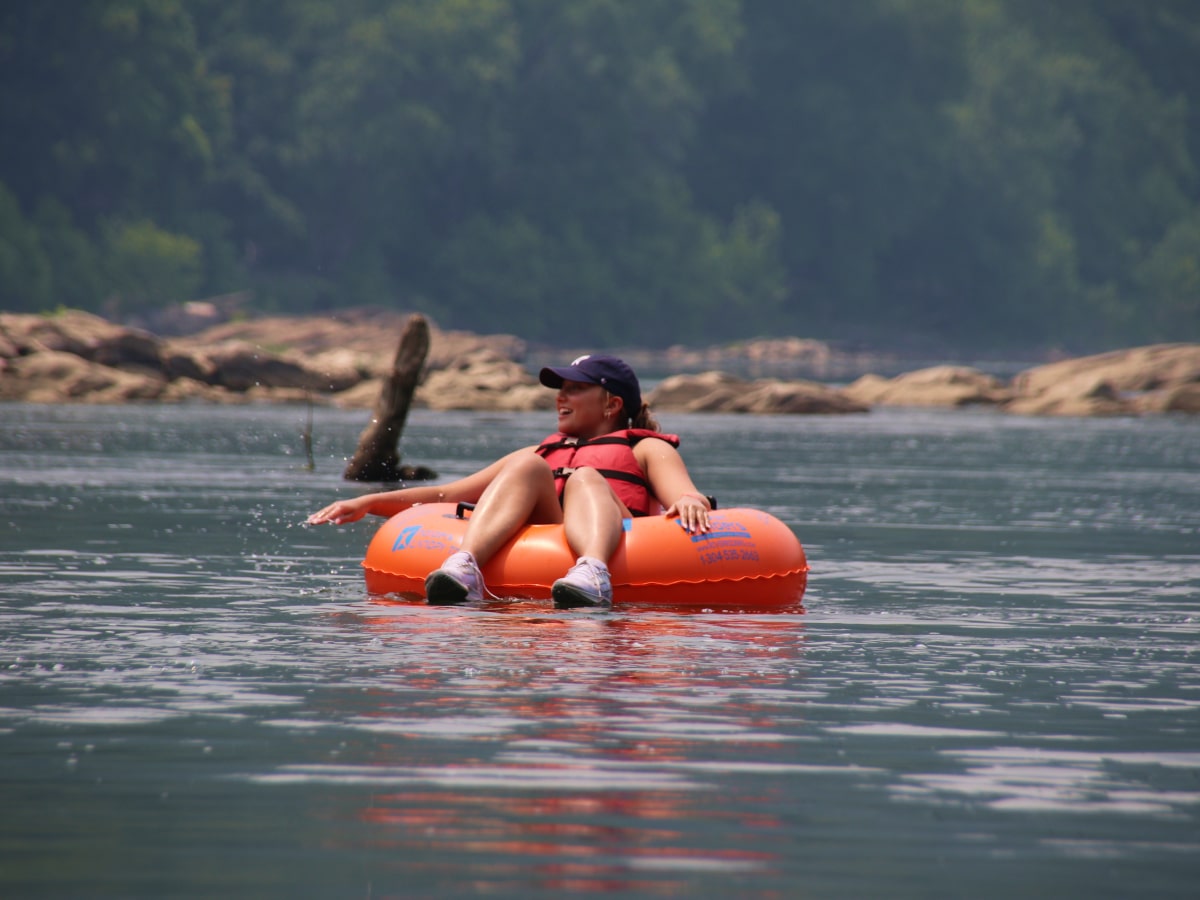 woman sitting in orange tube floating down the flat water of a river