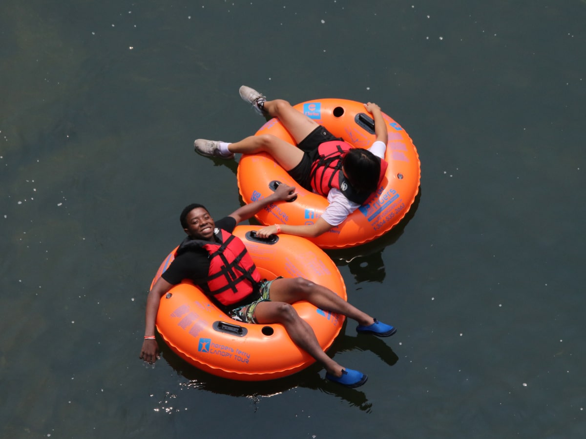 two boys sitting in orange tubes floating down the flat water of a river