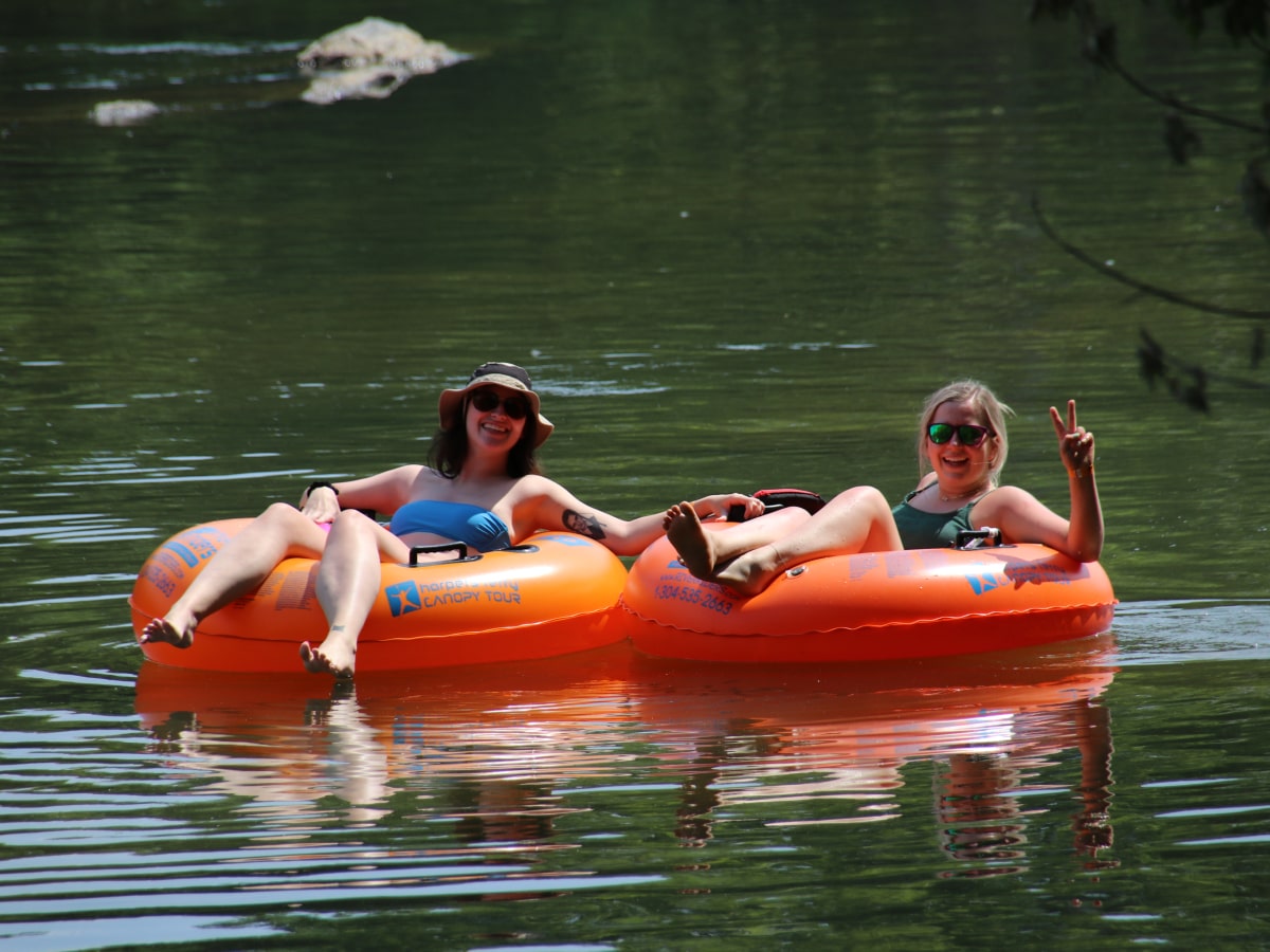 two women sitting in orange tube floating down the flat water of a river