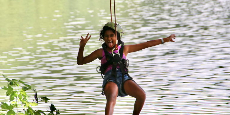 girl ziplinig through the tree with water in the background